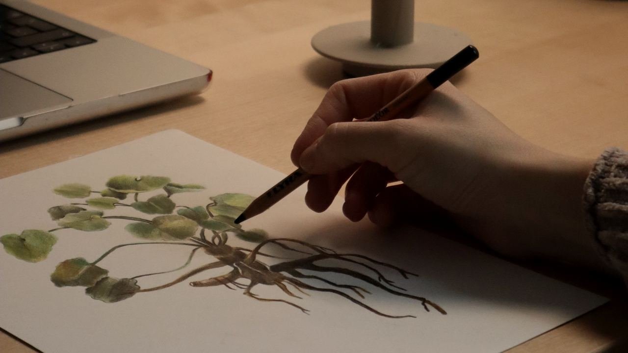 Mano dibujando sobre papel en un escritorio iluminado con una vela