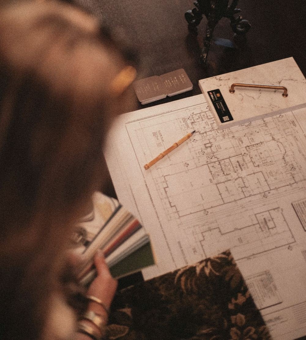 Over the shoulder of a designer at her desk, with floor plans, a pencil and color swatches