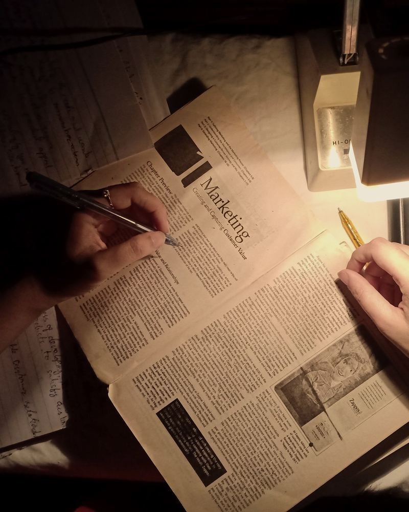 Hands taking notes on a marketing book under a desk lamp at night
