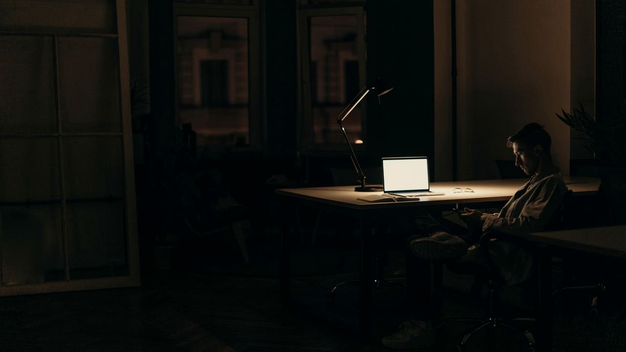 Alguien trabajando de noche frente a una laptop en una oficina oscura
