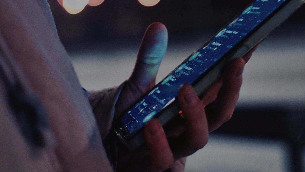 Una mano con un celular de noche entre luces de la ciudad